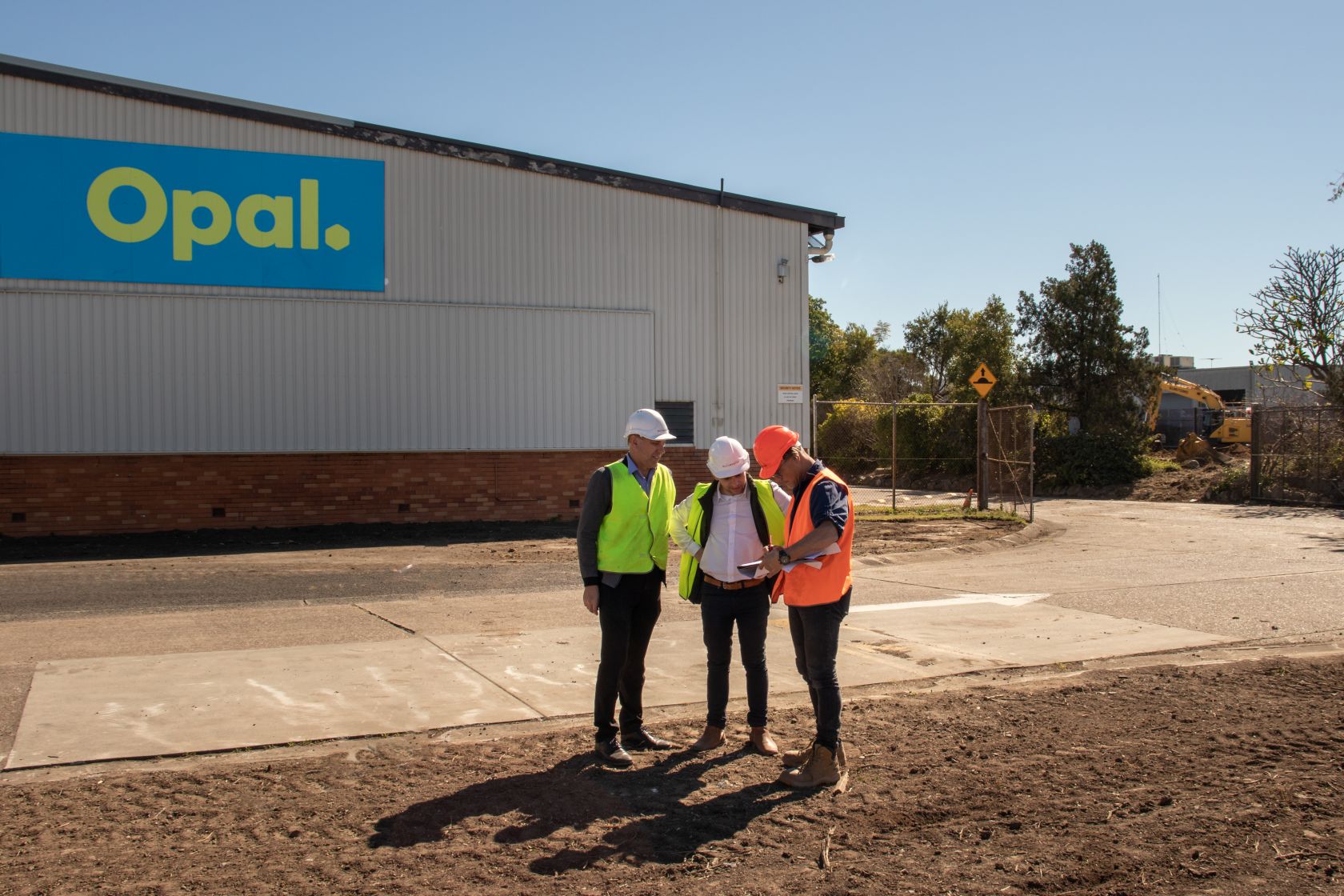 3 construction workers consult plans standing outside of Orora manufacturing plant